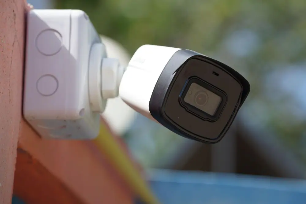 Біла вулична кулеподібна камера відеоспостереження з чорним об'єктивом і поворотним кріпленням, встановлена на цегляній стіні будинку