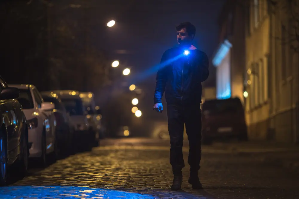 Мужчина освещает ночную улицу ручным LED-фонарем с синим лучом – выбор тактических моделей по типам и дальности