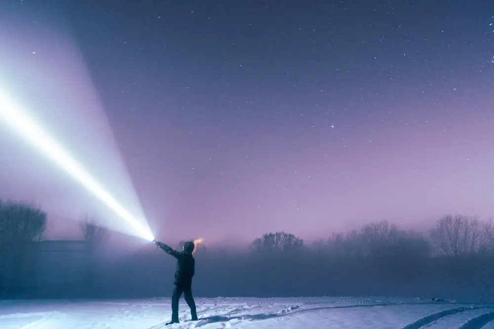 Мужчина в зимнюю ночь направляет мощный LED-фонарь в звездное небо – выбор поисковых моделей по типам и дальности