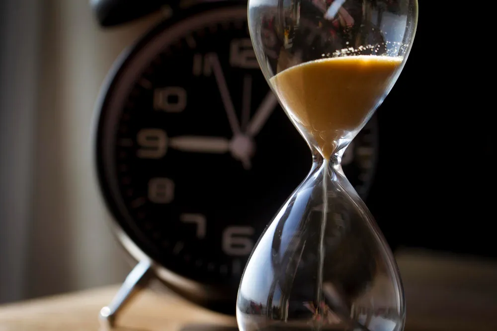 Пісочний годинник на передньому плані та розмитий циферблат на фоні, що символізують розрахунок часу автономної роботи ДБЖ